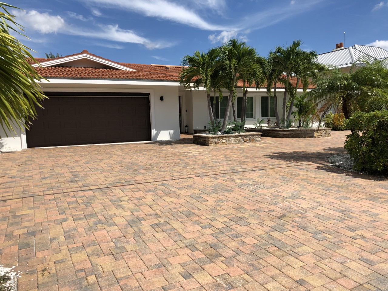 Single story house with paver driveway, palm trees