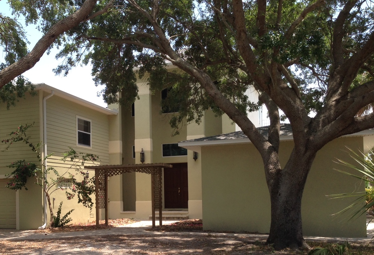 Two-story beige house with large oak tree
